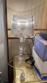 White ghost table lamp with transparent baroque design on a bedside table in a modern bedroom