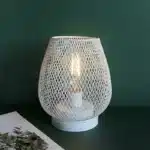 Decorative bird cage lamp with warm LED light, iron frame, and silk screen details on a bedside table