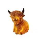 Whimsical cow table lamp with highland cattle design, casting a warm glow on a bedside table