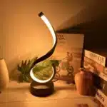 Modern desk lamp with adjustable arm and USB cable, glowing warmly on a wooden desk