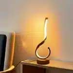 Modern desk lamp with adjustable arm and USB cable, glowing warmly on a wooden desk