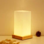 Modern table lamp with iron body and wood base illuminating a cozy bedroom