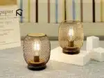 Battery table lamp with metal cage and warm LED glow on a wooden table