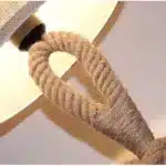 Vintage table lamp with hemp rope and iron base, emitting warm light on a bedside table