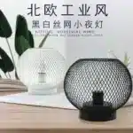 Decorative bird cage lamp with warm LED light, iron frame, and silk screen details on a bedside table