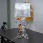 White ghost table lamp with transparent baroque design on a bedside table in a modern bedroom