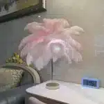 Ostrich feather table lamp glowing warmly on a bedside table in a cozy bedroom