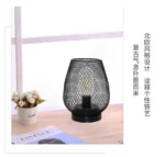 Decorative bird cage lamp with warm LED light, iron frame, and silk screen details on a bedside table