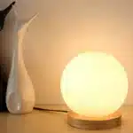 Modern table lamp with iron body and wood base illuminating a cozy bedroom