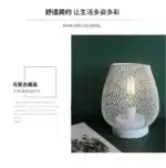 Decorative bird cage lamp with warm LED light, iron frame, and silk screen details on a bedside table