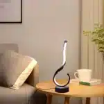 Modern desk lamp with adjustable arm and USB cable, glowing warmly on a wooden desk